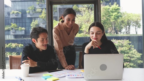 Three business professionals discussing charts and reports while analyzing information on laptop during collaborative office meeting.