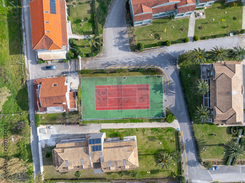 Aerial Top Down View of Green and Red Tennis Court Surrounded by Resort Villas in Corfu Greece