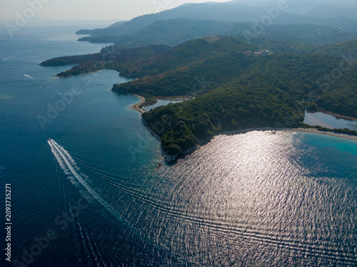 Aerial view of a motorboat navigating deep blue waters along a lush green coastline.