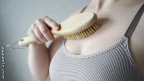 Static Shot Of Woman Dry Brushing Skin On Chest With Wooden Brush In Close Up Wellness Routine Against Neutral Indoor Background.