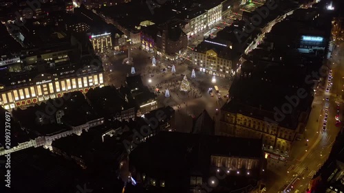 Aerial night orbit of Dam Square in Amsterdam, Netherlands, with a Christmas tree, illuminated cone trees, the National Monument, department stores and the Royal Palace during the holiday season.
