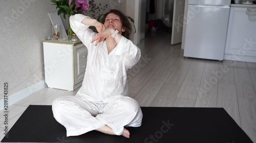 Static Shot Of Woman Performing Seated Stretching And Arm Movements On Yoga Mat In Bright Home Living Room With Kitchen Background.