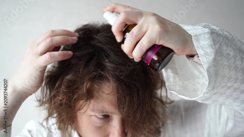 Static Shot Of Woman Spraying Hair Product And Combing Messy Curly Hair With Fingers Against Plain Indoor Bathroom Wall At Home.