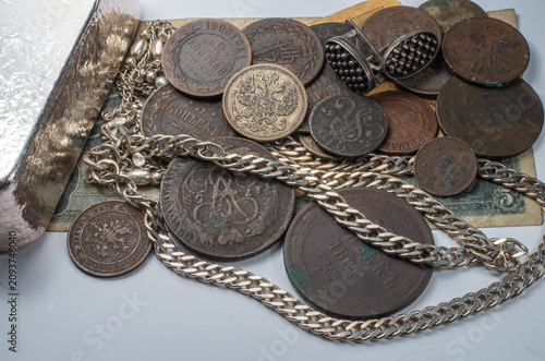 A collection of antique coins, silver jewelry, vintage currency, and a silver bar arranged together, showcasing historical treasures and numismatic heritage.