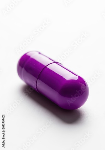A vibrant purple medicinal capsule placed on a clean white surface, highlighting health, medication, and wellness themes, vibrant, purple, tablet
