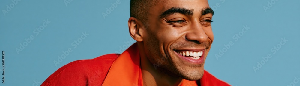 Fototapeta premium Candid smiling male portrait in orange coat on sky blue background for website banner and advertising design