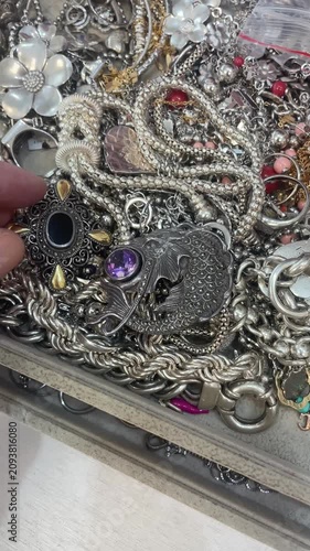 Hand browsing the silver vintage jewellery tray at the thrift shop