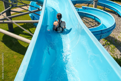 Obraz na płótnie Teen girl sliding down blue water slide at outdoor pool in summer