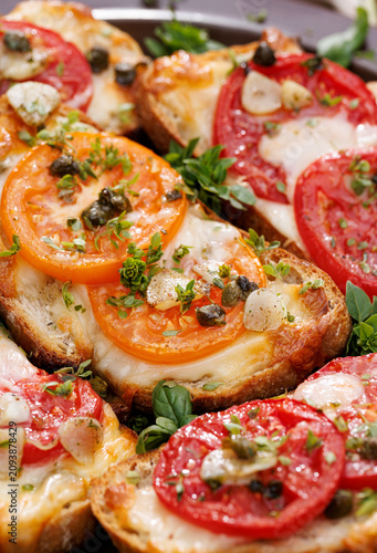 Grilled sourdough bread sandwiches, bruschettas with mozzarella and grana padano cheese, tomatoes, capers and garlic seasoned with aromatic herbs, close-up view