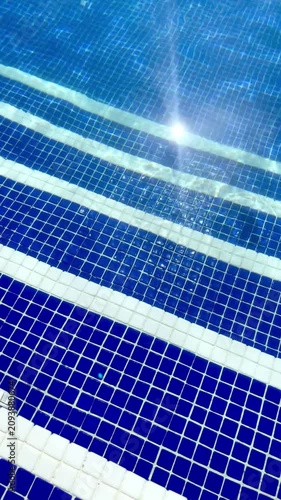 sunlight reflecting on the clear blue water over the tiled steps of a swimming pool creating a sparkling effect and beautiful patterns
