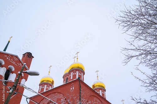 Εκτύπωση καμβά A low-angle view of a red brick Orthodox church with golden onion domes and cros