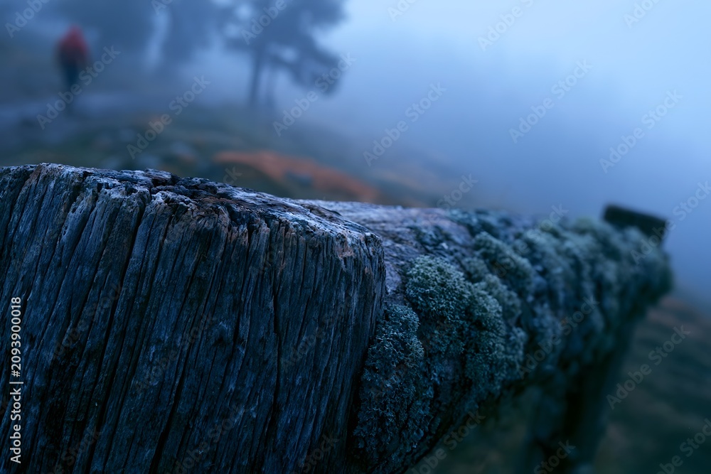 Fototapeta premium Weathered fence post in sharp macro against foggy valley