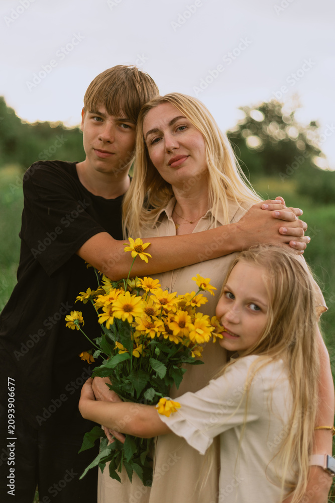Fototapeta premium Mother and children embracing in a field with a bouquet of yellow flowers