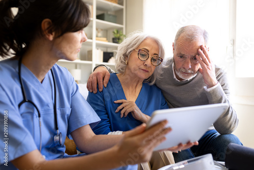 Doctor showing bad news on tablet to worried senior couple at home