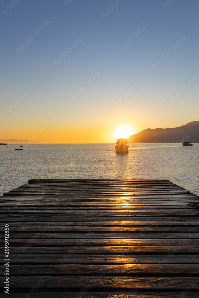 Naklejka premium Beautiful sunrise at São Francisco Beach Pier in São Sebastião, Brazil, with calm sea, golden reflections, and panoramic views of Ilhabela and Ubatuba. 