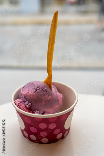 scoop of purple berry ice cream in a paper cup with a wooden spoon