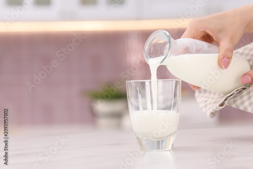 Принти на полотні Woman pouring fresh milk into glass at light table in kitchen, closeup