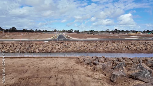 New roads and rock-lined drainage channel run through cleared, subdivided land prepared for house construction in outer suburban Werribee, Melbourne Australia. Urban development, land subdivision