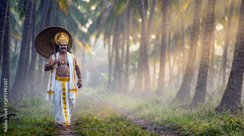 Mythological King Mahabali walking through a misty coconut grove holding a traditional leaf umbrella during Onam festival in Kerala, beautiful morning sun rays with copy space.