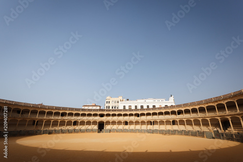 Sunlit horseshoe shaped decks of seating surround the empty bullfight ring in the arena of Ronda, Spain.