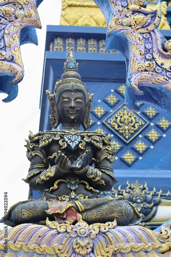 Obraz premium Seated meditating deity statue with folded hands against ornate temple wall