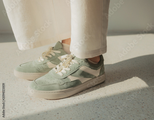 Standing person showing green sneakers with cream accents on light floor from left side view in natural light