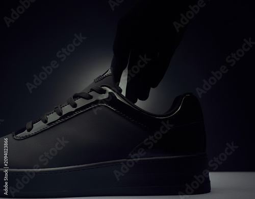 Close-up View of a Black Sneaker with Thick Sole on a Leg in a Dark Environment from a Low Angle