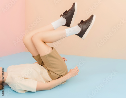 Woman lying on colorful floor with legs raised, wearing khaki shorts and dark brown sneakers, in a studio setting, from a creative viewpoint