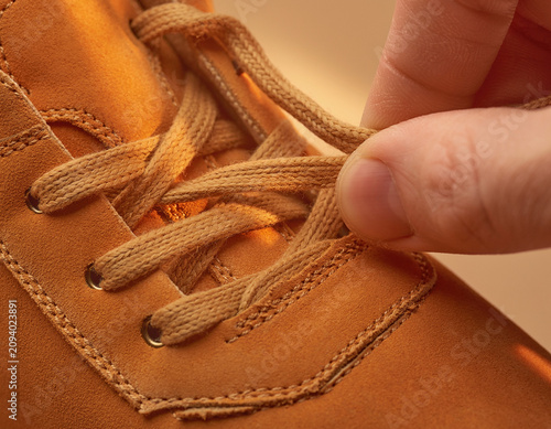 Close-up of hand adjusting laces on brown leather boot in studio environment with focus on quality and craftsmanship
