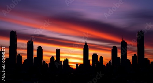 City skyline silhouettes against vibrant sunset sky with clouds