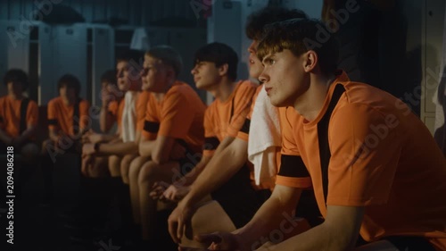Close Up of Young Football Player in Orange Jersey in Locker Room. Boy Listens With Intense Concentration to Coach Post Training Briefing. Concentration, Tactical Understanding, and Dedicated Mindset.