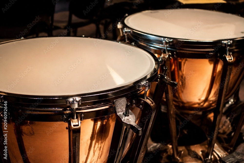Fototapeta premium A pair of polished copper kettledrums with taut drumheads gleaming under focused stage lighting.