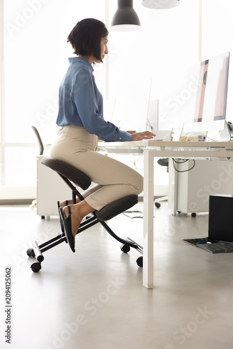 Foto Employee working at computer in office seated on ergonomic kneeling chair with upright posture, showing healthy and correct position