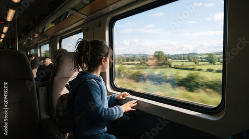 Young girl looking out train window at green landscape  
