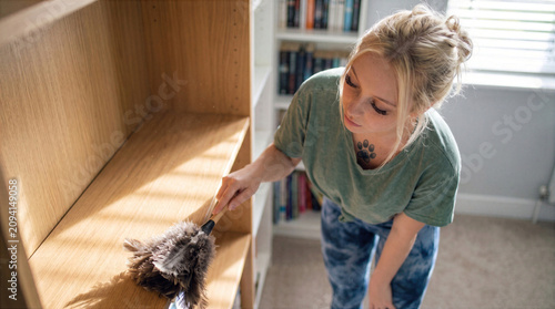 Young Woman Dusting Wooden Shelves During Home Cleaning