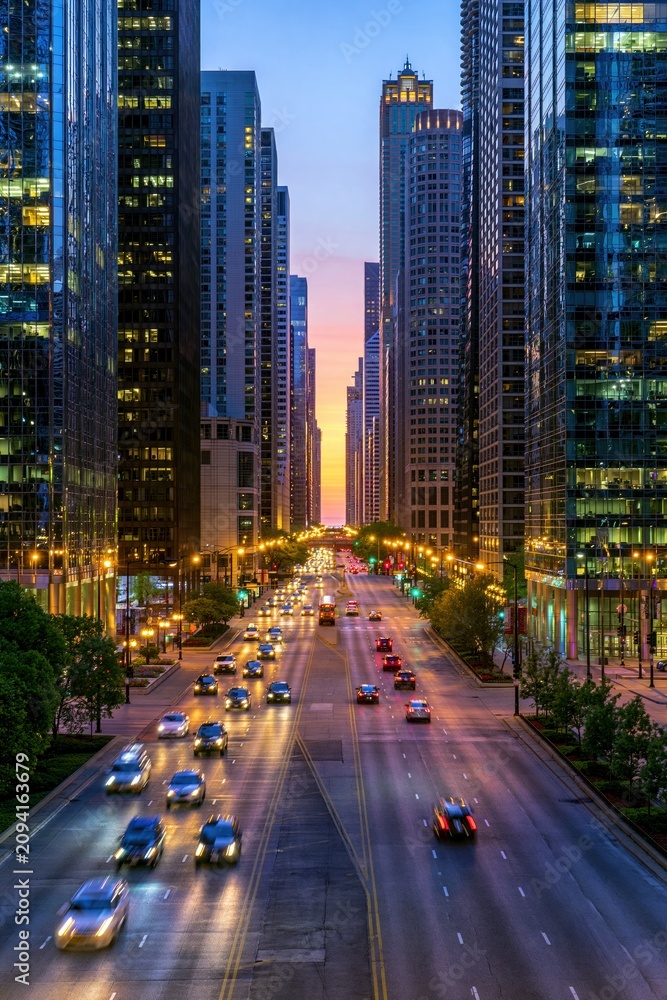 Obraz premium Urban downtown street corridor at twilight with tall glass skyscrapers and glowing vehicle lights for metropolitan lifestyle and business branding