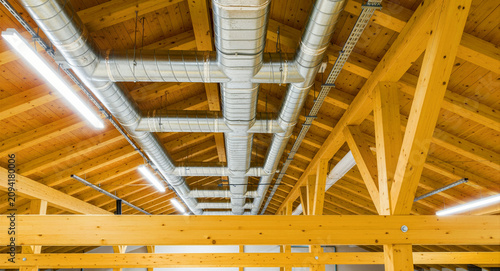Ventilation pipes on a wooden ceiling. Modern HVAC system with timber beams and LED lighting. Engineering concept for sustainable building design.