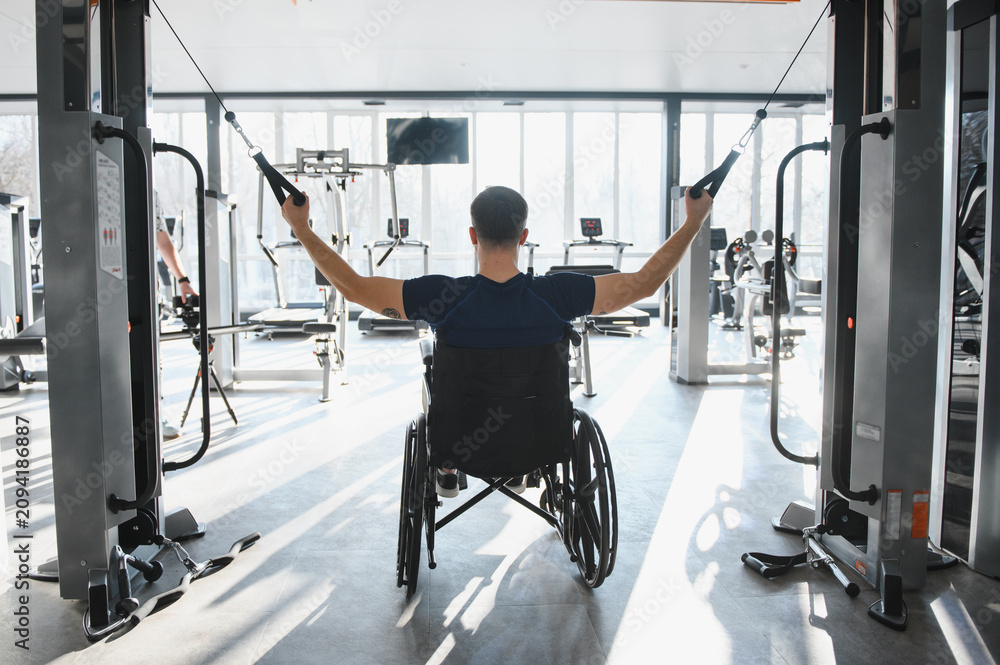 Fototapeta premium Man in wheelchair exercising arms with cable machine in gym