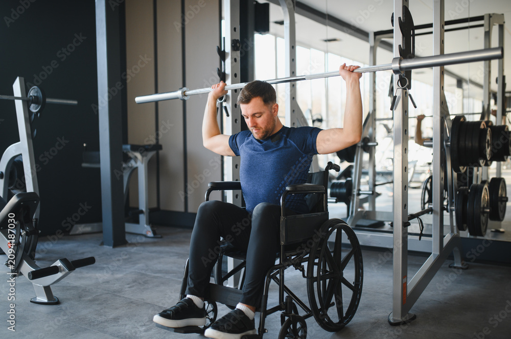 Fototapeta premium Man with disability lifting weights in wheelchair at gym for rehabilitation