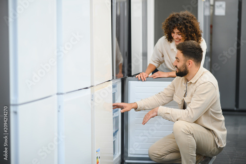 Couple choosing refrigerator in electronics store examining home appliances