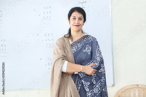 Confident indian woman teacher smiling while standing in front of a whiteboard e in classroom, Education india.