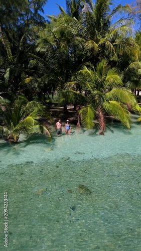 Explore the beauty of Koh Kood, Thailand, as two travelers wander through calm, turquoise waters surrounded by swaying palm trees. Experience paradise in every step.