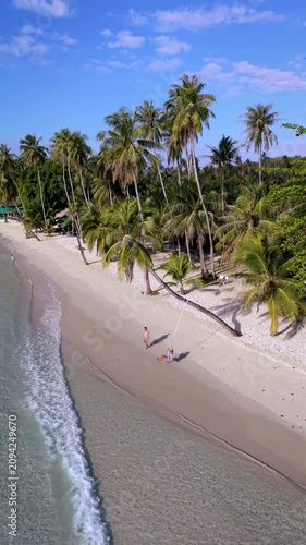 Relax on the pristine shores of Koh Kood Thailand, where soft sands meet crystal-clear waters. A couple enjoys tranquil moments surrounded by palm trees and vibrant nature in this tropical paradise.