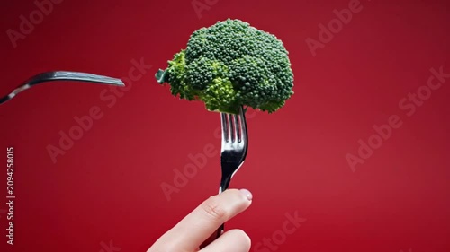 Creative shot of broccoli florets impaled by forks against a vibrant red background symbolizing healthy eating