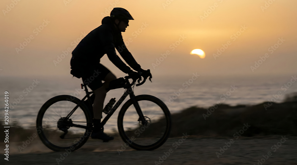 Obraz premium Silhouetted cyclist on a coast path with crescent eclipse sun