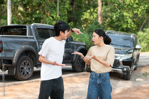 Two people involved in a roadside dispute argue beside their cars, showing shock and frustration after a sudden accident.