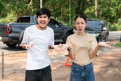 Two people involved in a roadside dispute argue beside their cars, showing shock and frustration after a sudden accident.