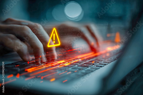 Hands typing on laptop with warning symbol on screen