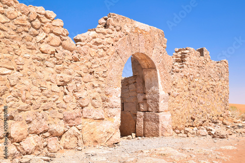 Fotografie The ancient stone gate arch of the Roman fort Castellum Tisavar and the Sahara Desert, Ksar Ghilane, Tunisia