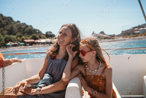Mother and daughter share a joyful moment while on a boat ride during a summer vacation. The mother smiles warmly as her daughter leans close, enhancing their bond and happiness.